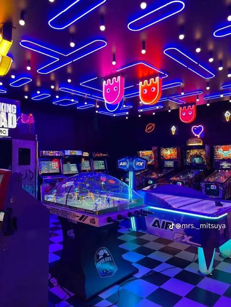 Sala de juegos arcade decorada con múltiples letreros neón en techo y paredes