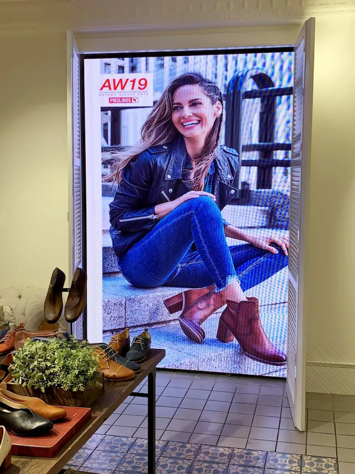 Pantalla LED vertical en tienda de calzado mostrando publicidad de moda femenina