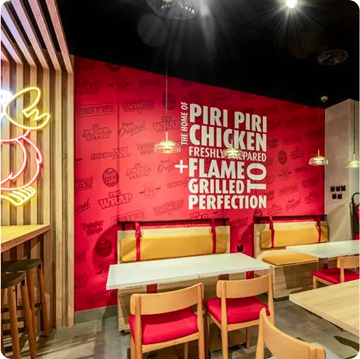 Vinilo en pared roja con texto Piri Piri Chicken en restaurante con diseño moderno y bancas amarillas